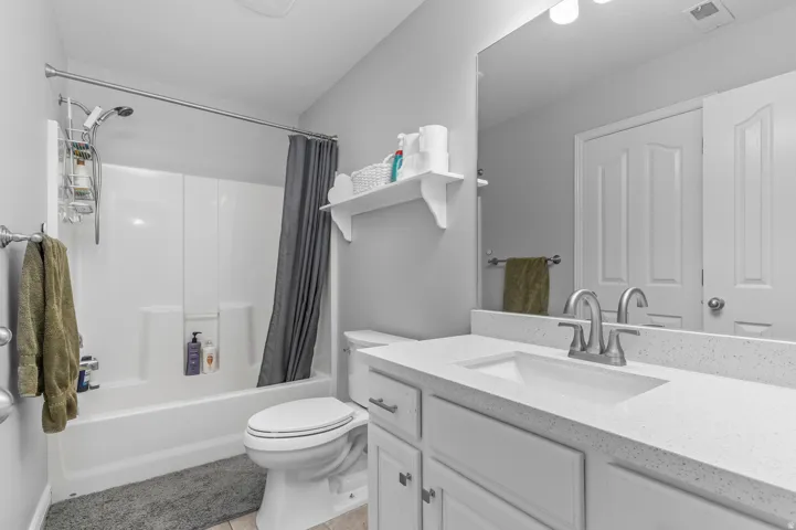 White vanity with integrated sink and chrome faucet, large vanity mirror, built-in shelving, and a combination tub/shower