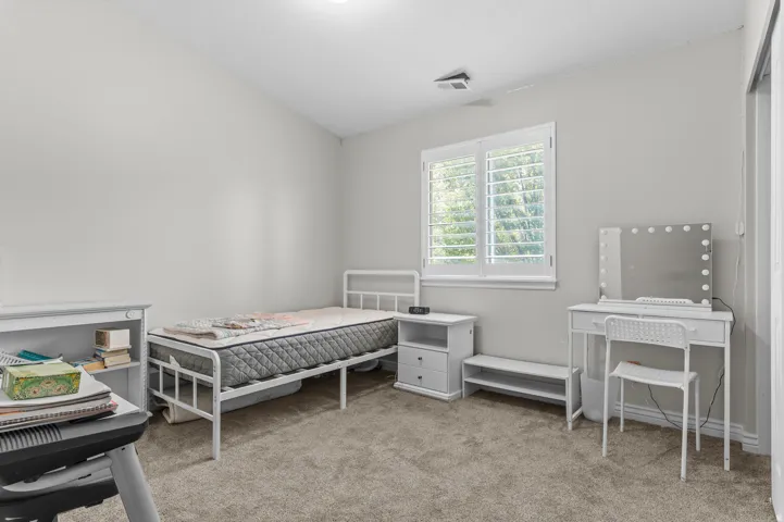 Bedroom with vaulted ceiling, neutral carpet, and a window featuring white plantation shutters