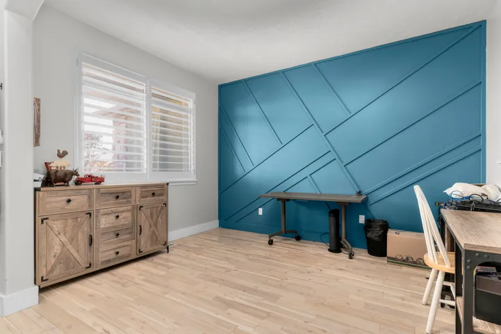 Accent wall with geometric paneling, wood-finish flooring, and window with plantation shutters