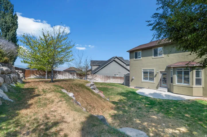 Expansive backyard featuring a concrete patio, mature tree, and a rock wall