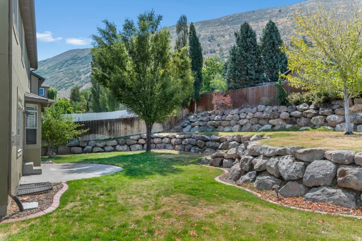 Expansive yard featuring a concrete patio, tiered rock retaining walls, and mature trees