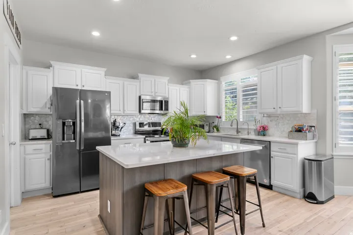 Modern kitchen featuring light wood-finish flooring, white cabinetry, a center island with a light-toned countertop, and stainless steel appliances