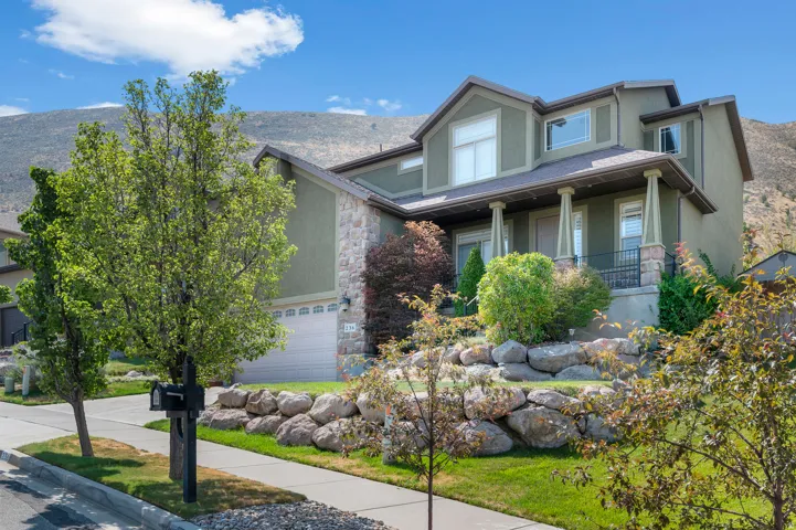 Two-story dwelling featuring a covered porch with columns, a two-car garage, and a retaining wall with rock landscaping
