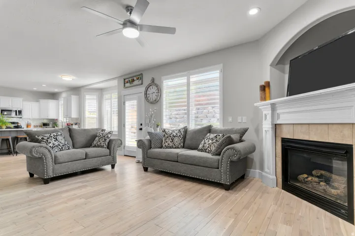 Recessed lighting, ceiling fan, wood-finish flooring, built-in fireplace, and kitchen with white cabinetry