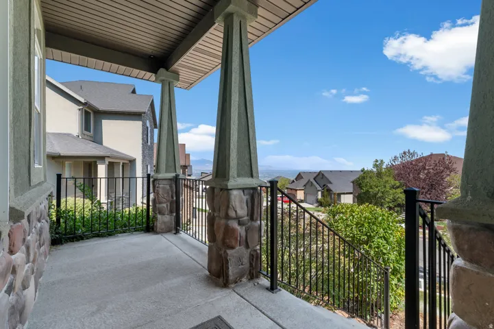 Covered front porch with concrete flooring and stone-clad pillars, featuring a wrought iron railing