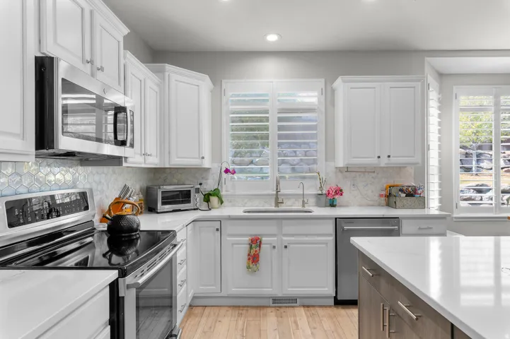 White shaker cabinetry, stainless steel appliances, light wood-finish flooring, white countertops, and plantation shutters