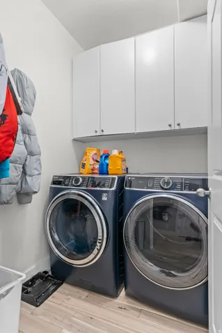 White upper cabinetry, wood-finish flooring, and built-in laundry appliances