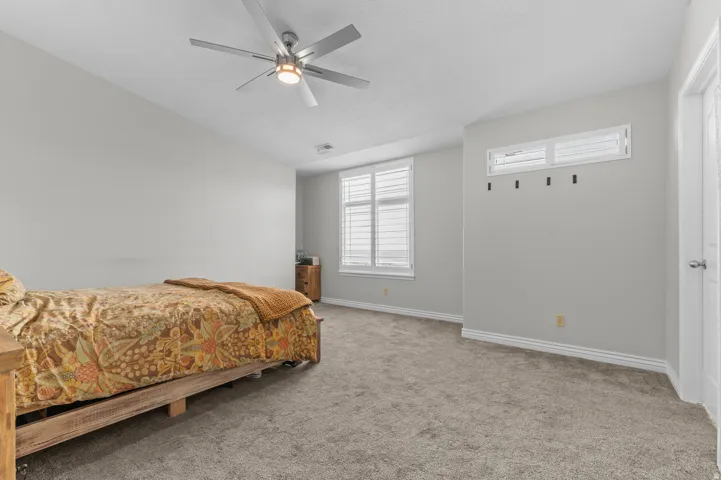 Neutral-toned walls with carpet flooring, featuring a ceiling fan with integrated lighting, a window with horizontal blinds, and a built-in shelf with decorative hooks