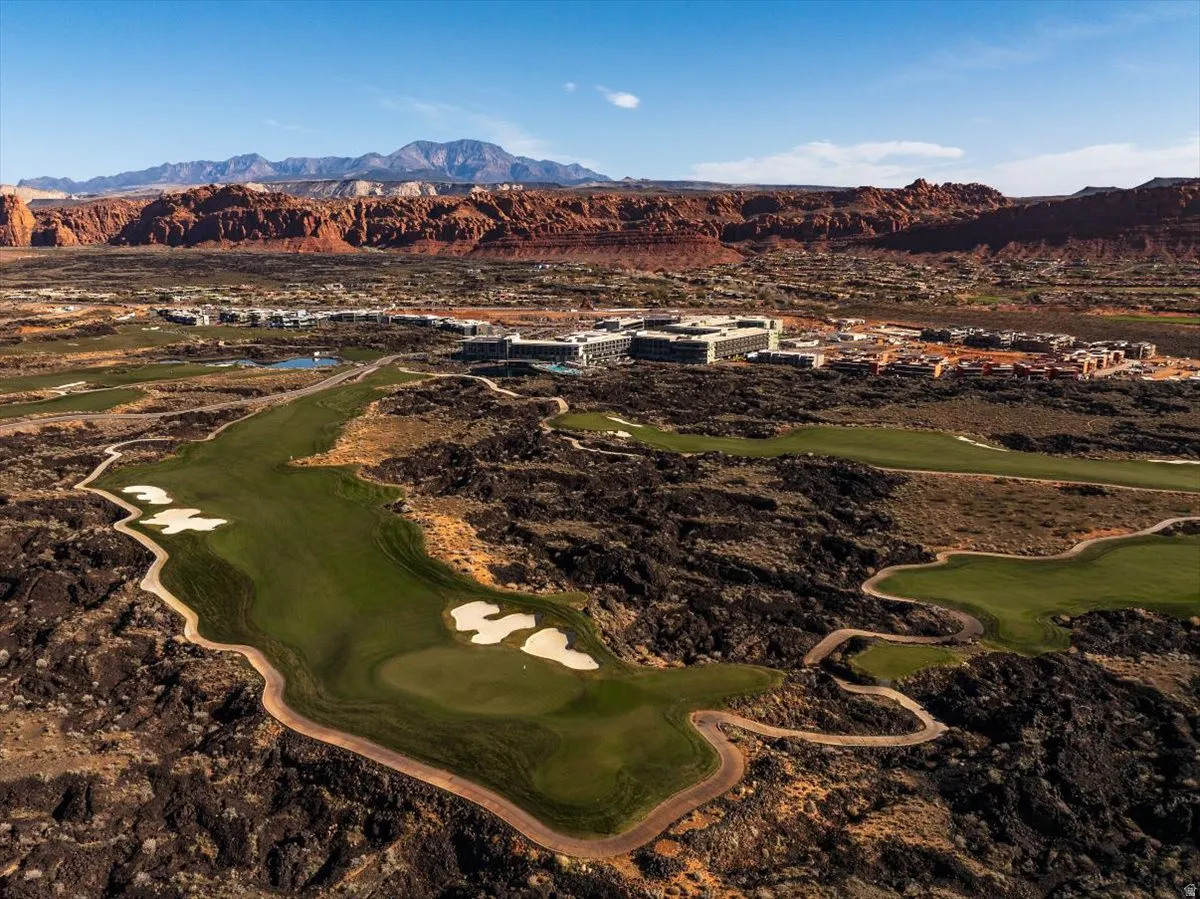 Expansive green golf course, surrounded by natural desert landscaping, with distant red rock formations and mountains under a clear sky