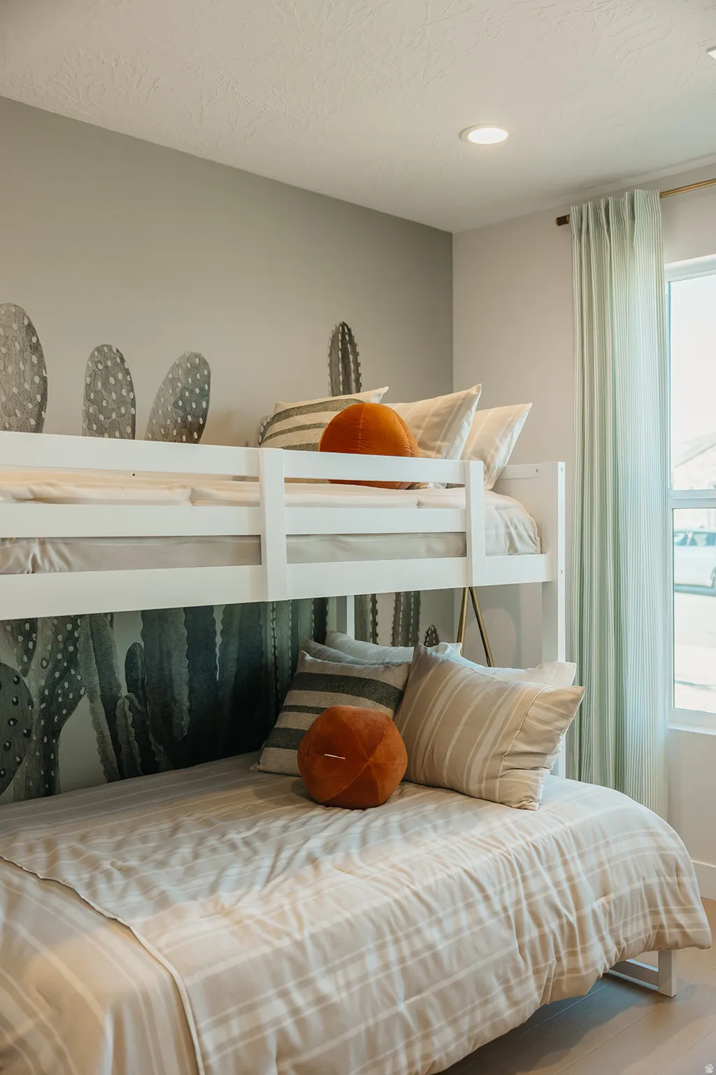 Recessed ceiling lighting, bunk bed frame, cactus-themed accent wall, and wood-finish flooring