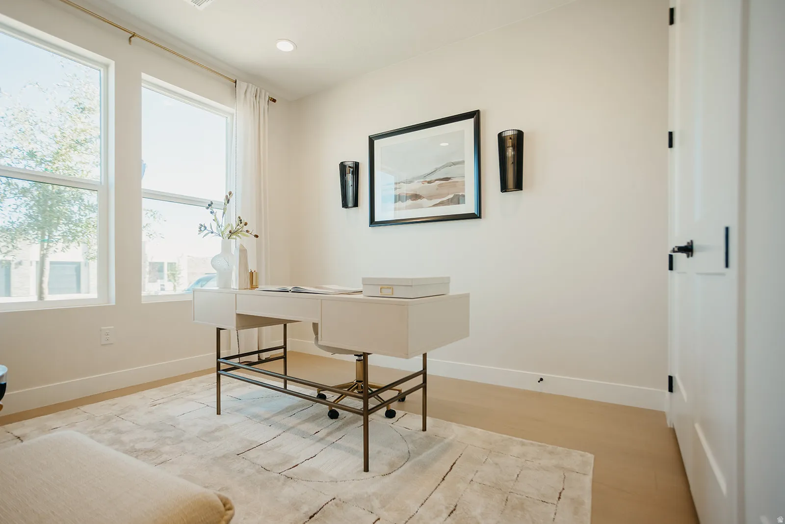Abundant natural light from multiple windows, light wood-finish flooring, white walls, recessed lighting, and a white paneled door with black hardware