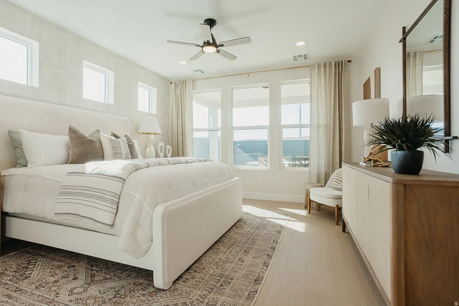 Light wood-finish flooring, ample natural light from multiple windows, recessed lighting, and a ceiling fan with integrated lighting