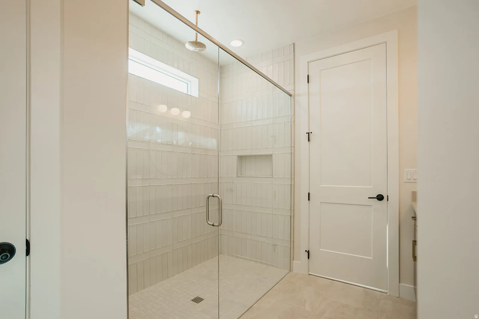 Glass-enclosed shower with a linear transom window, tiled walls, a built-in shower niche, and a rain shower head