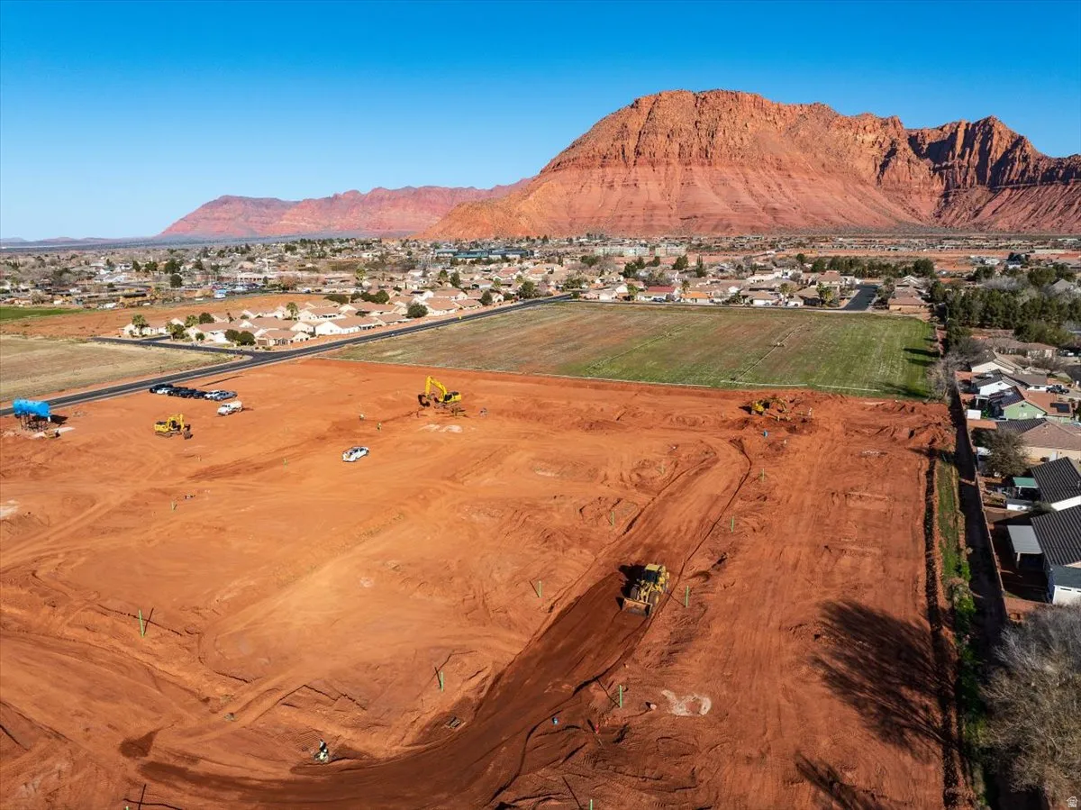 Expansive undeveloped land parcel with red earth, surrounded by a residential community and natural rock formations
