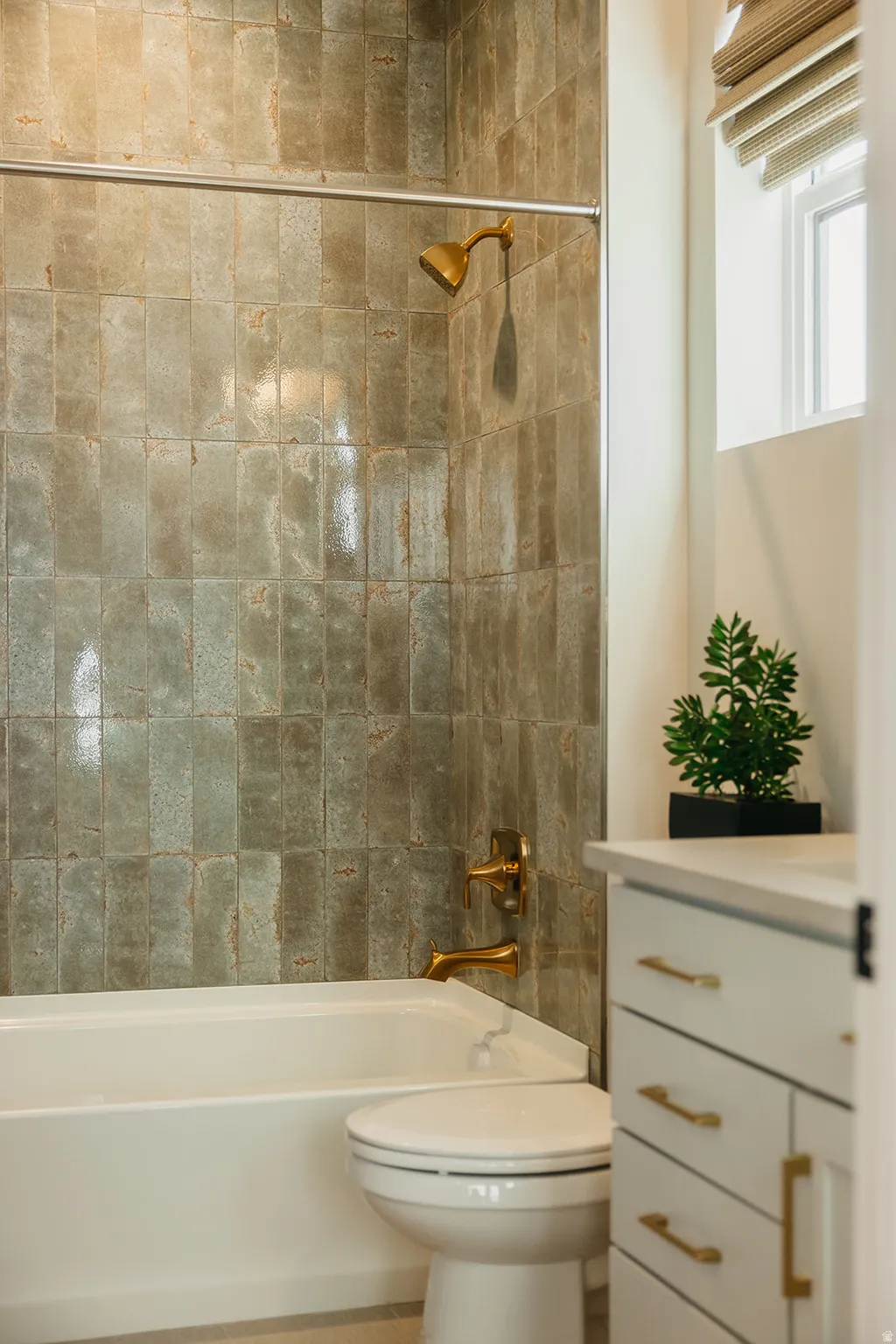 Bathtub with full-height tile surround, gold-tone fixtures, and white vanity with gold-tone hardware