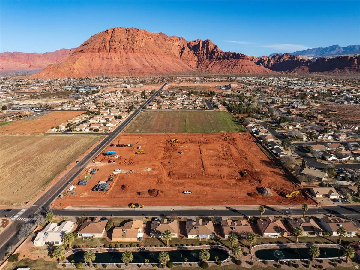 Expansive development site featuring red earth, surrounded by established residential areas, with a prominent mountain backdrop