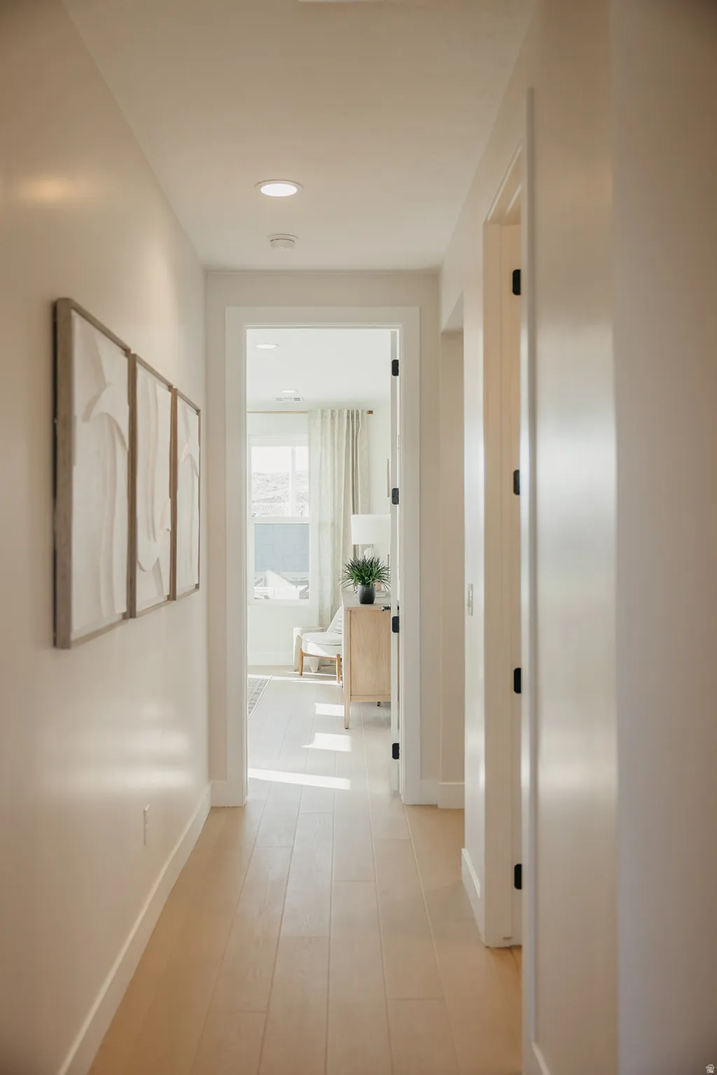 Recessed ceiling lighting illuminates a hallway with light wood-finish flooring