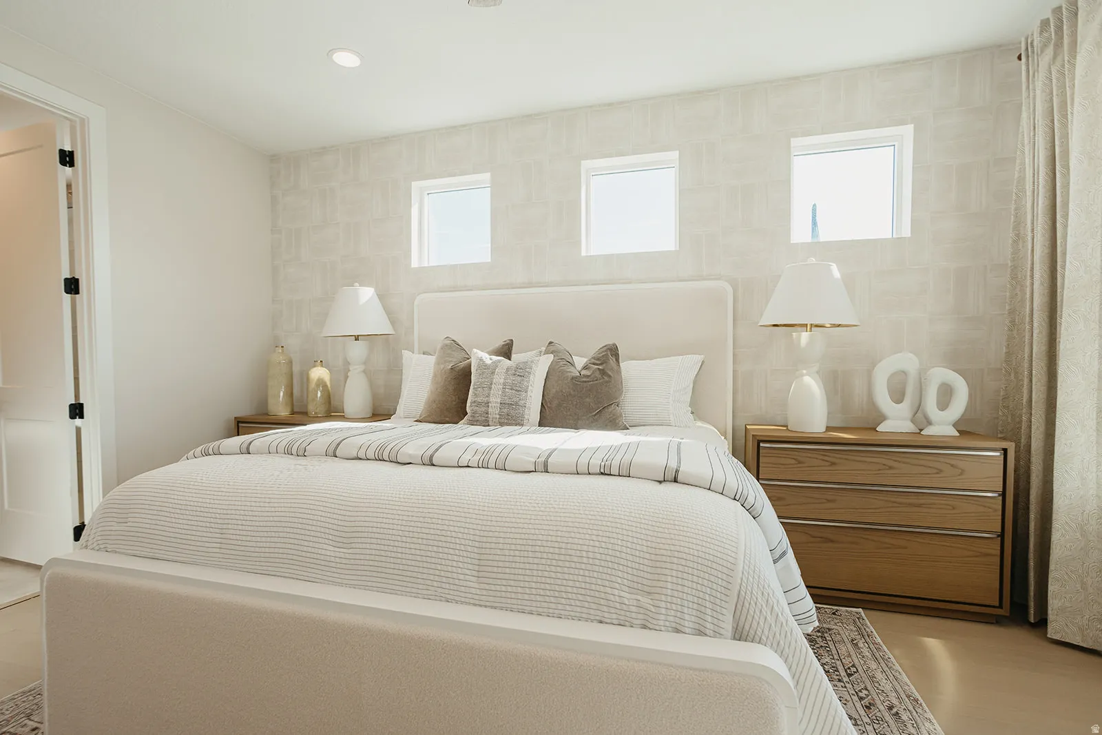 Recessed lighting, patterned wall covering, three transom windows, a solid panel interior door, and a built-in wood-finish dresser with metal accents