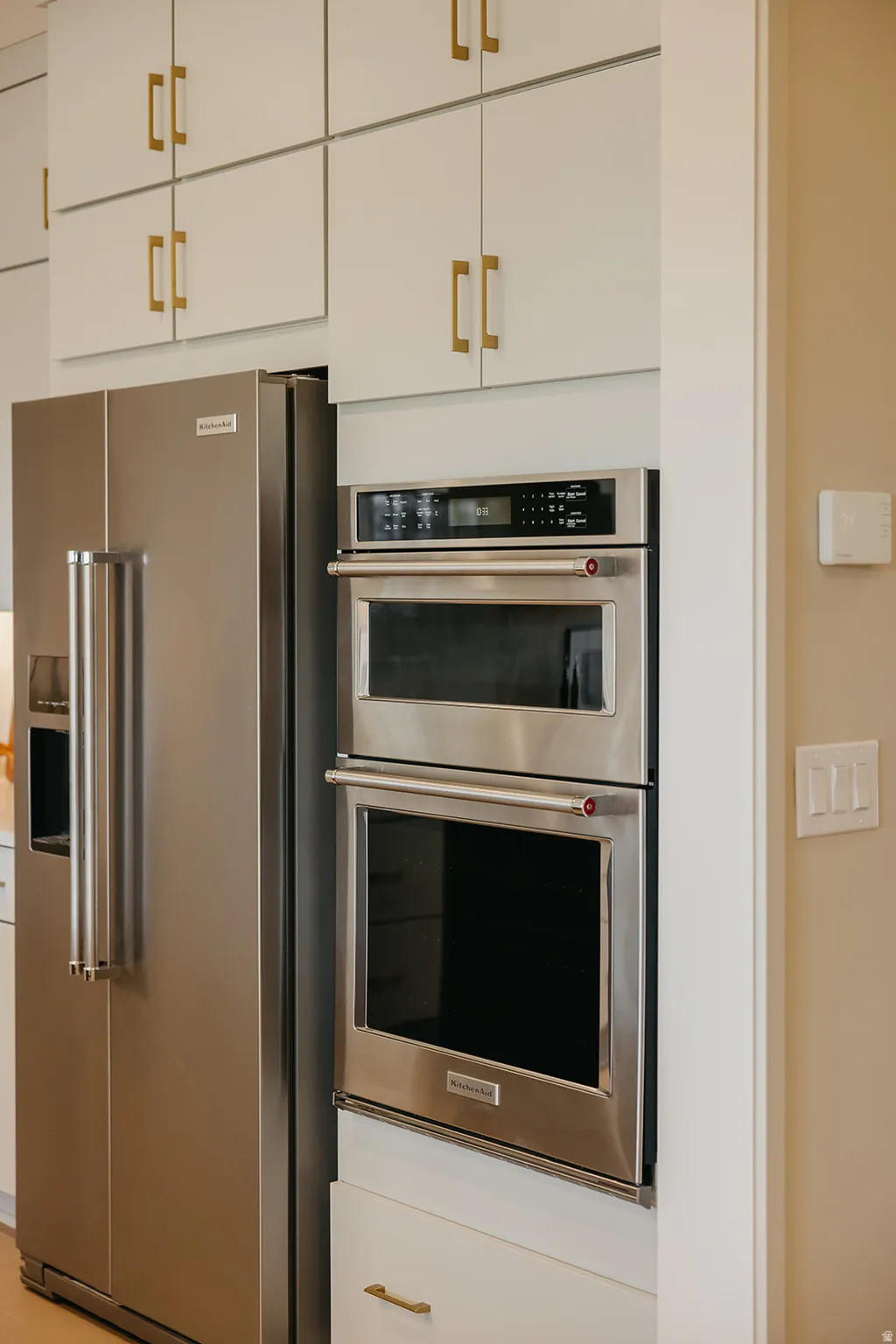 Stainless steel refrigerator, integrated double wall ovens, built-in cabinetry, and gold-finish hardware