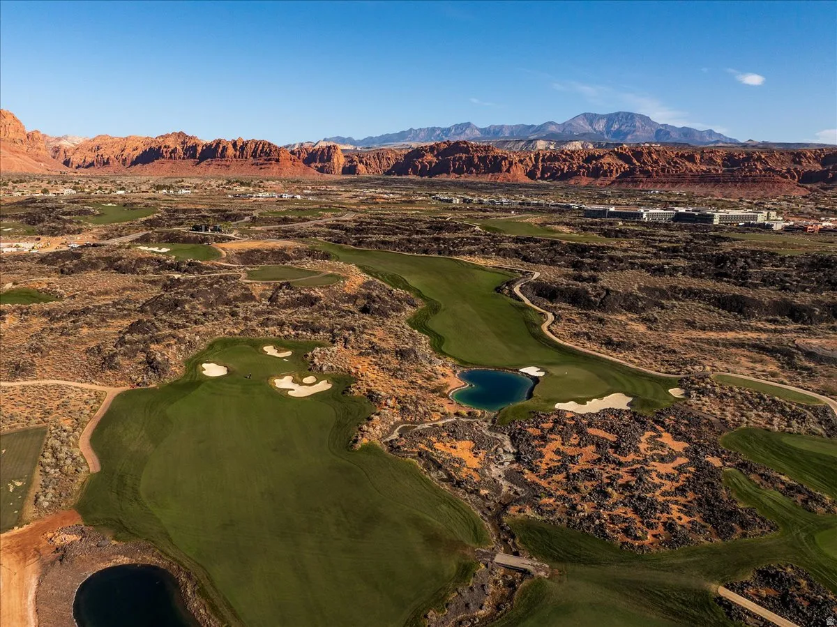 Expansive golf course with manicured greens, water features, and sand traps, set against a backdrop of distant red rock formations and mountains