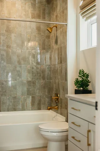 Bathtub with full-height tile surround, gold-tone fixtures, and white vanity with gold-tone hardware