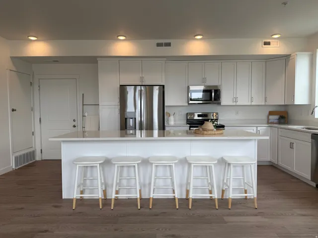 Kitchen featuring white cabinetry, stainless steel appliances, a center island with countertop seating, recessed lighting, and wood-finish flooring