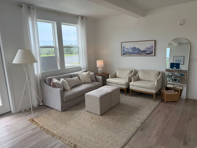White walls with exposed ceiling beam, wood-finish flooring, and large windows