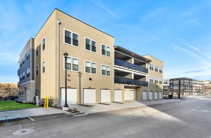 Multi-story building featuring a stucco and horizontal siding exterior, multiple garage doors, black framed windows, and balconies with dark railings