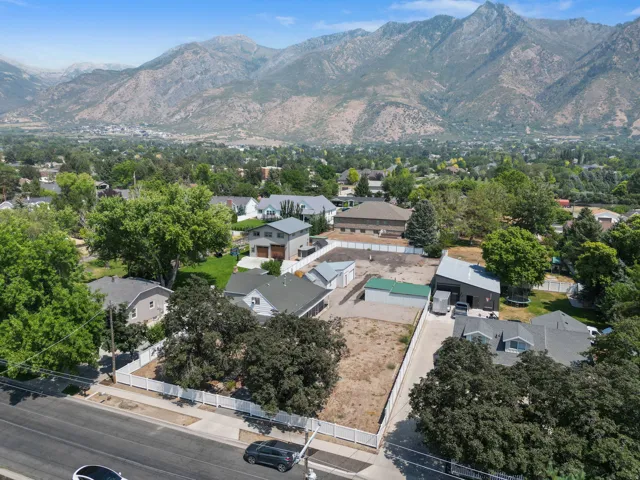 Expansive lot with mountain backdrop, established trees, and a white fence perimeter