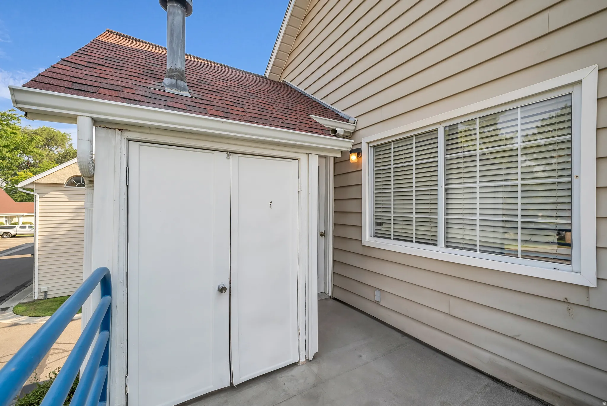 Exterior siding in a neutral tone, white-framed window, red-shingled roof, and a built-in outdoor storage unit