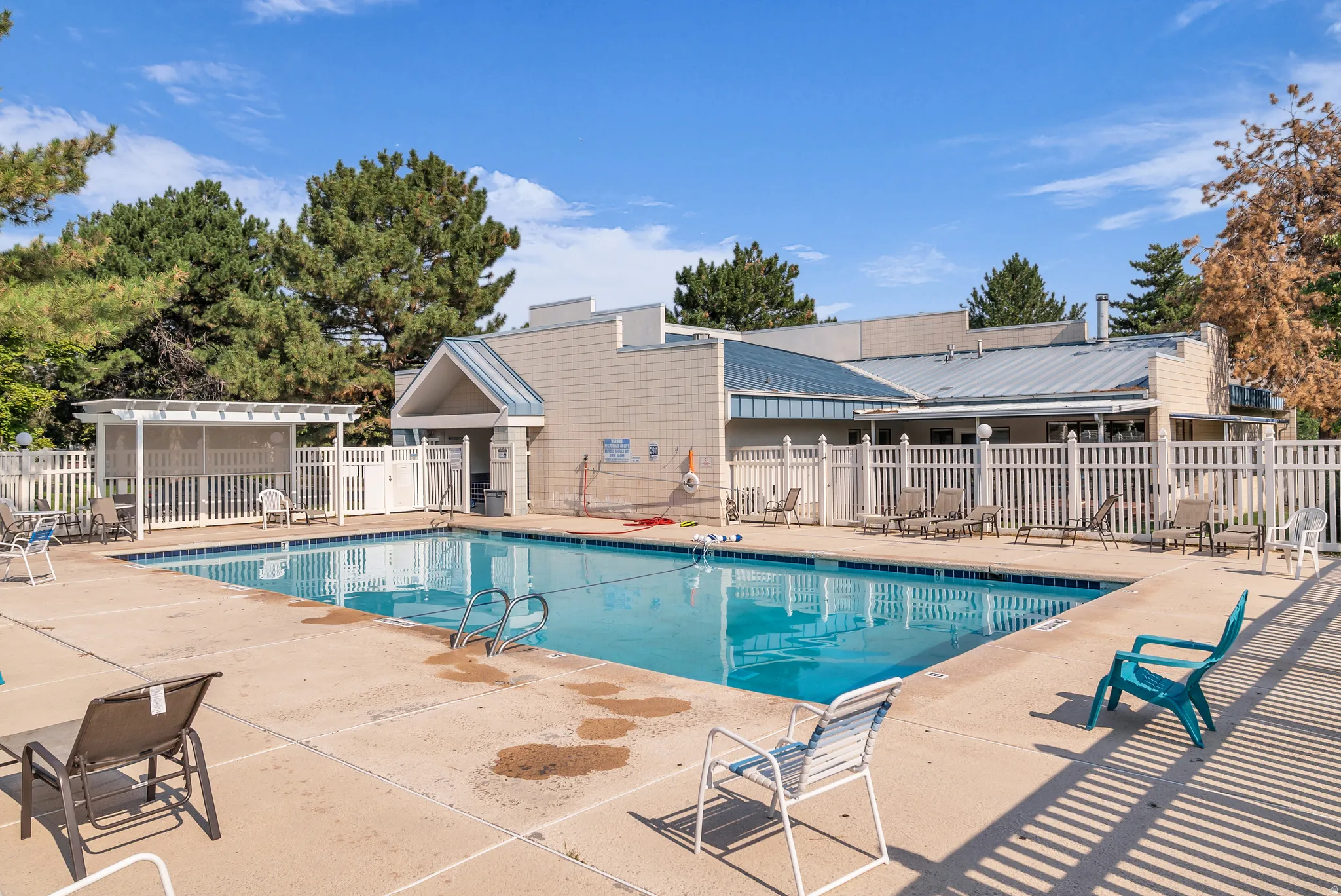 Outdoor swimming pool with integrated steps, surrounding concrete decking, white picket fencing, and an adjacent covered structure