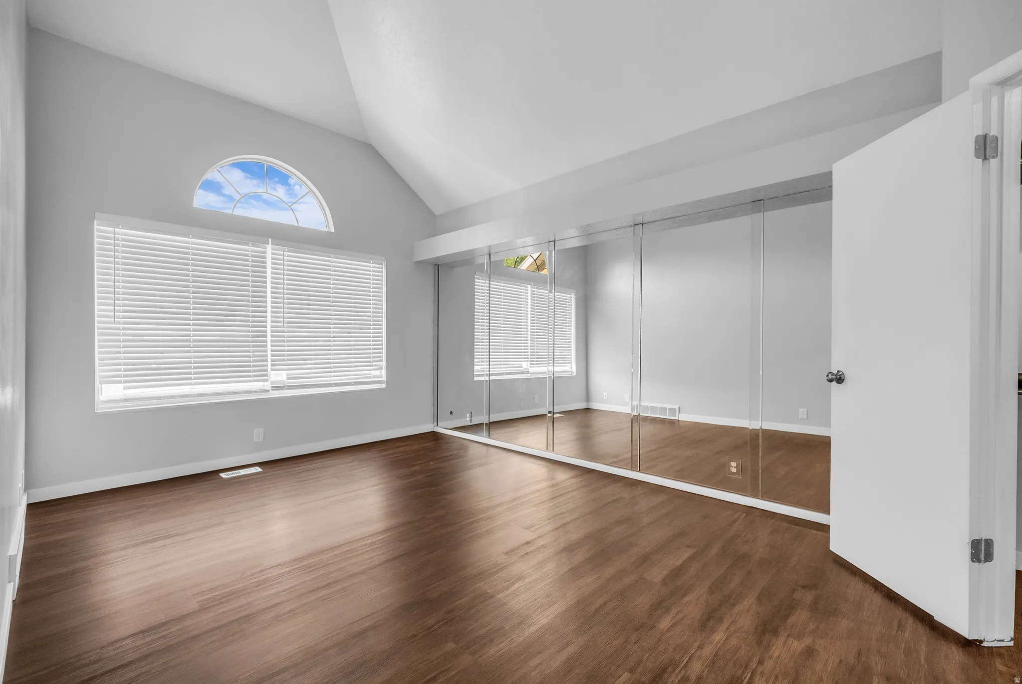Vaulted ceiling, arched window accent, wood-finish flooring, full-wall mirrored closet doors, and white interior door