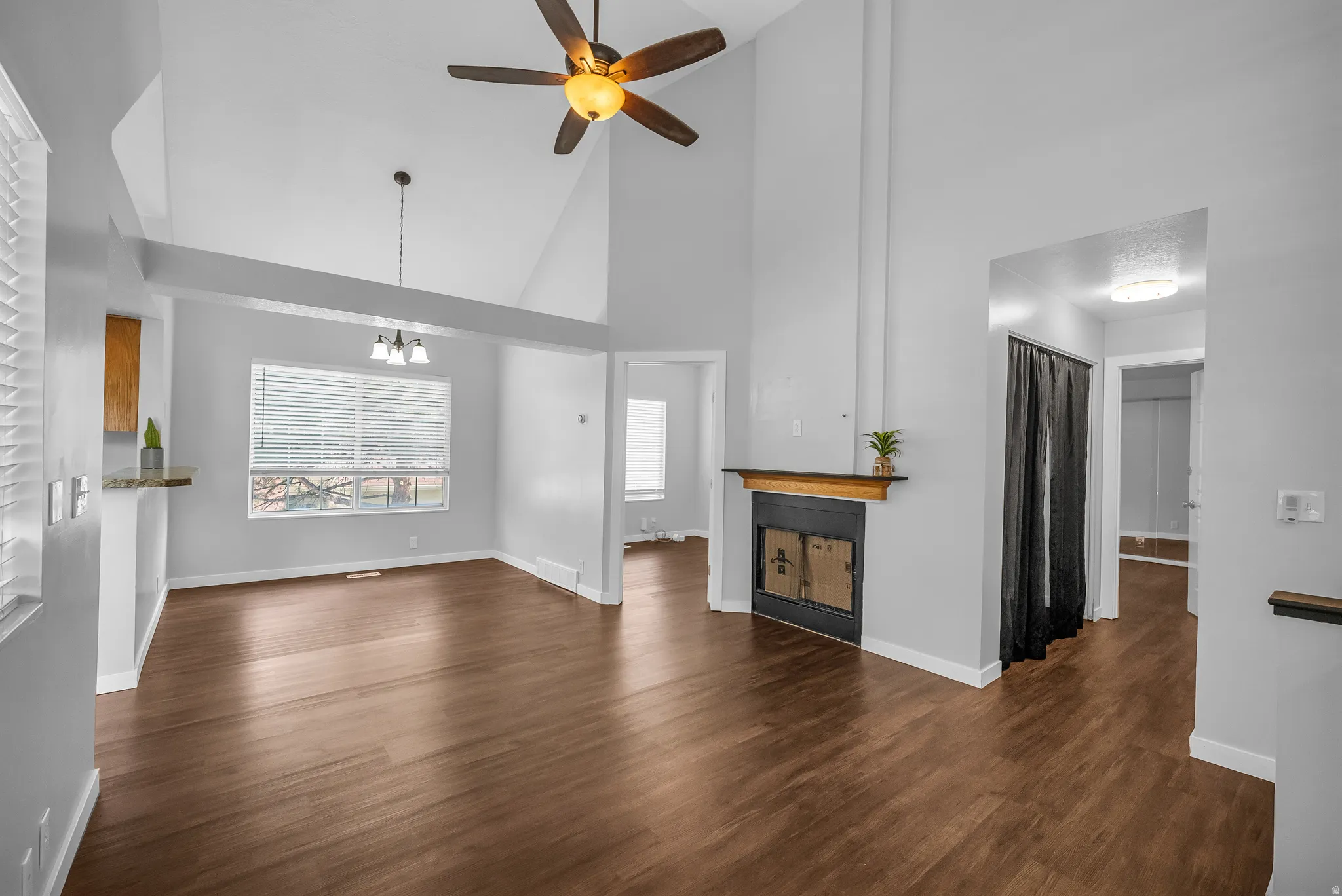 Vaulted ceiling with a ceiling fan, wood-finish flooring, built-in fireplace, and a window with horizontal blinds