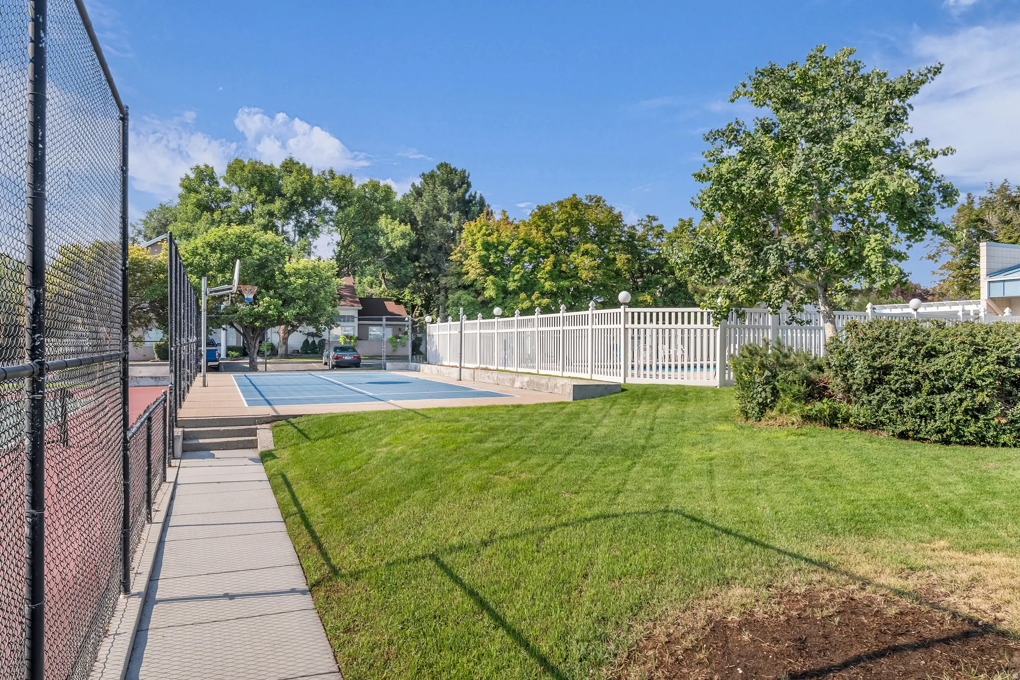 Multi-sport court, expansive lawn, concrete walkway, white picket fence, and mature trees