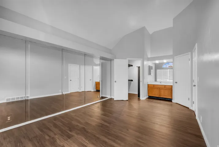 Vaulted ceilings, wood-finish flooring, mirrored closet doors, built-in vanity with wood cabinetry, and an arched window with blinds