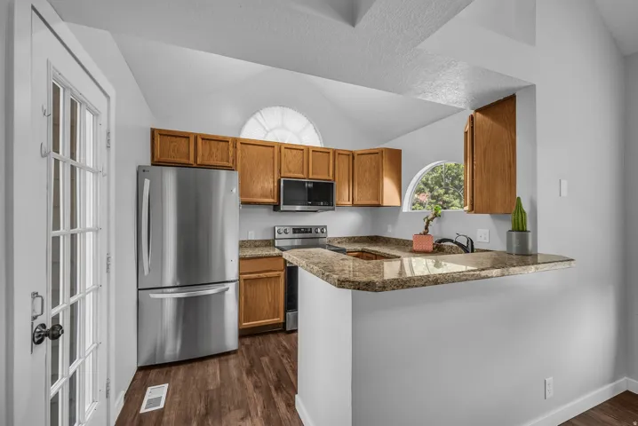 Kitchen featuring wood-finish cabinetry, stainless steel appliances, a breakfast bar, and vaulted ceilings with an arched window