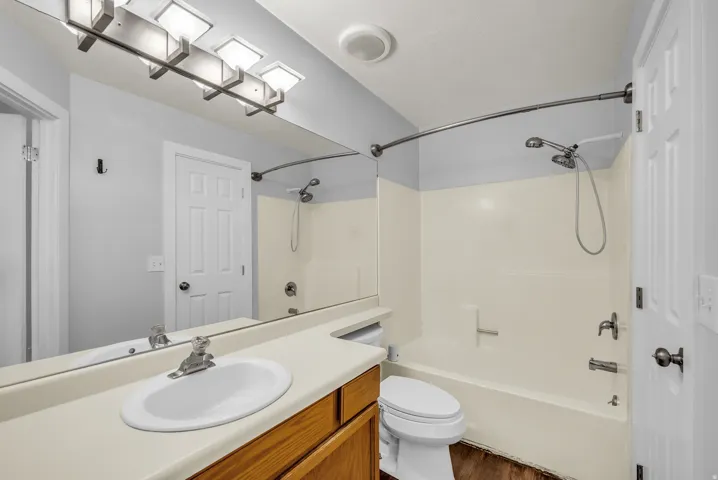 Bathroom featuring a single vanity, integrated sink, wood-finish cabinetry, and a shower/tub combination with a curved shower rod