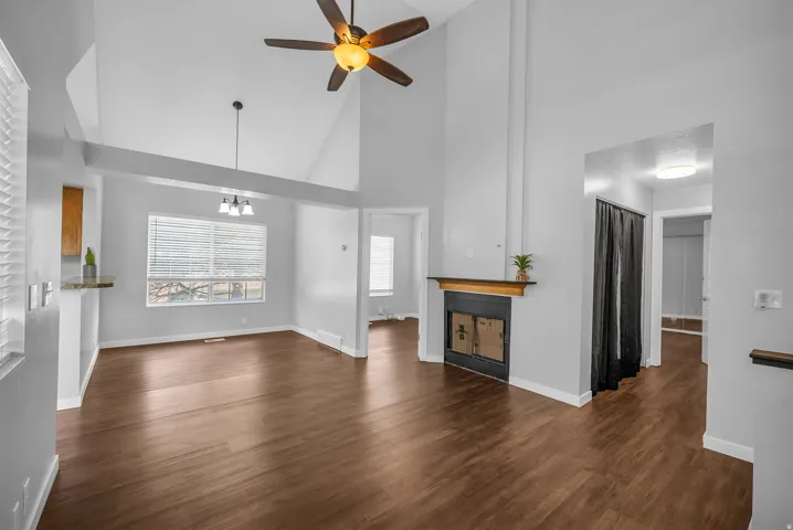 Vaulted ceiling with a ceiling fan, wood-finish flooring, built-in fireplace, and a window with horizontal blinds