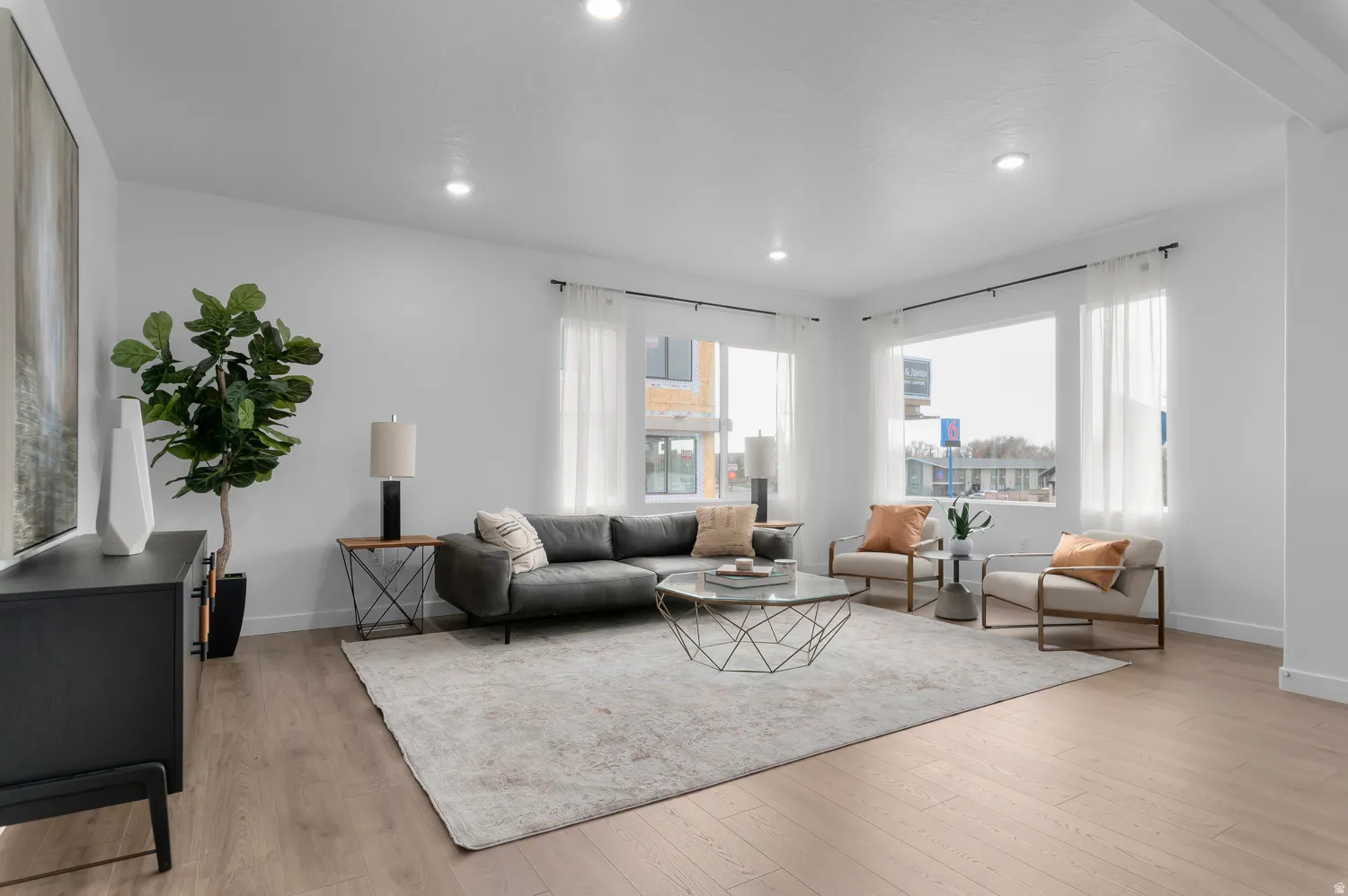 Recessed lighting, wood-finish flooring, white walls, and multiple windows with sheer white curtains