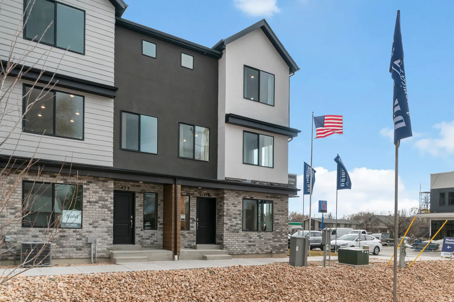Contemporary townhome exterior featuring multi-toned siding and brick, dark window frames, and prominent entryways