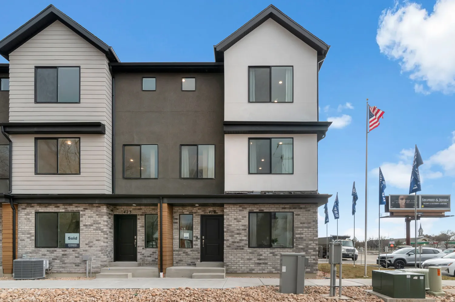 Contemporary townhome exterior featuring light-colored siding, dark stucco accents, and a grey brick facade