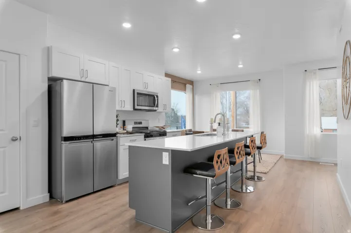 Kitchen featuring wood-finish flooring, stainless steel appliances, white cabinetry, a gray island with a white countertop, and recessed lighting
