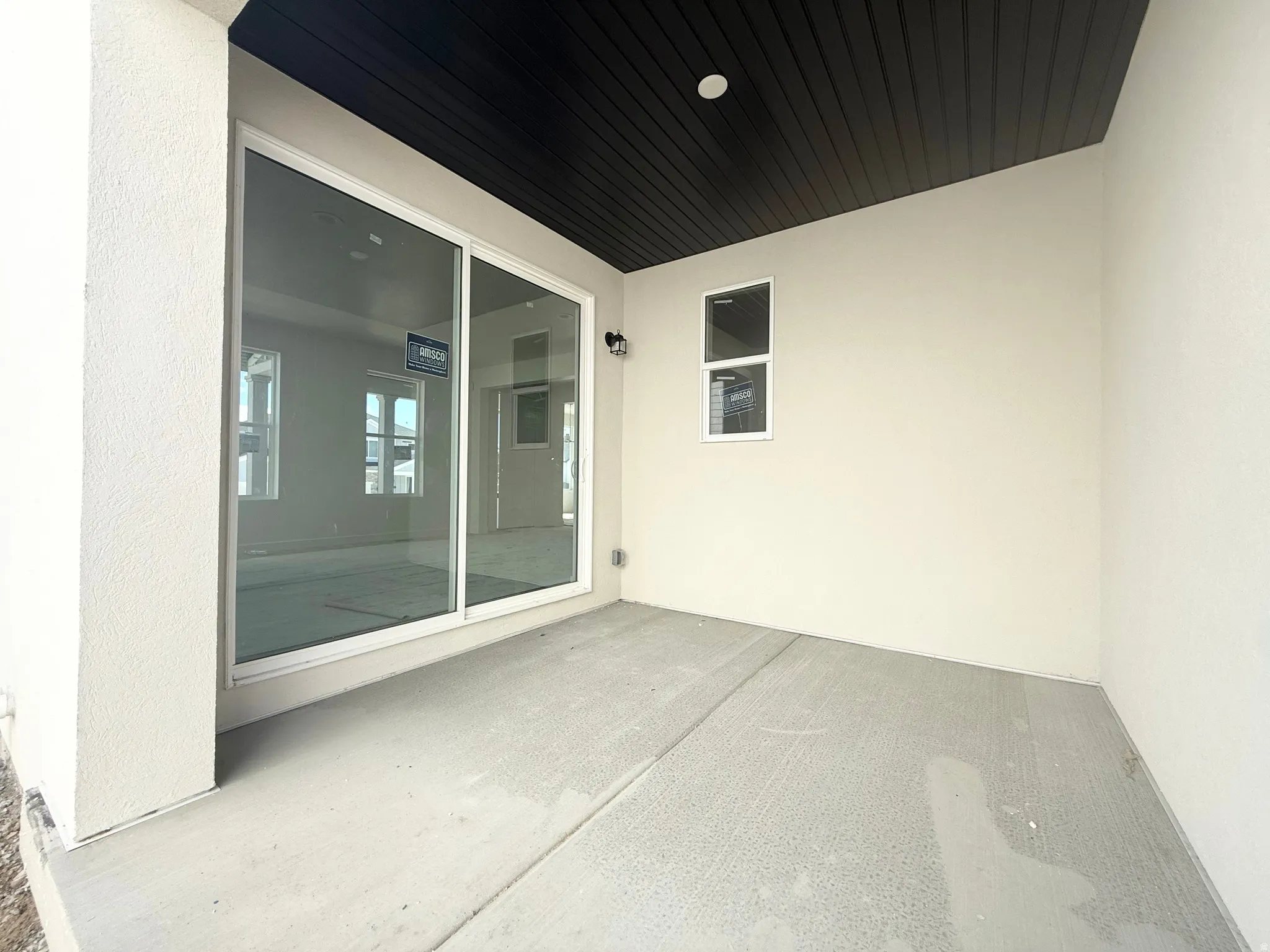 Covered patio with a concrete surface, white stucco exterior, and a dark wood-finish ceiling
