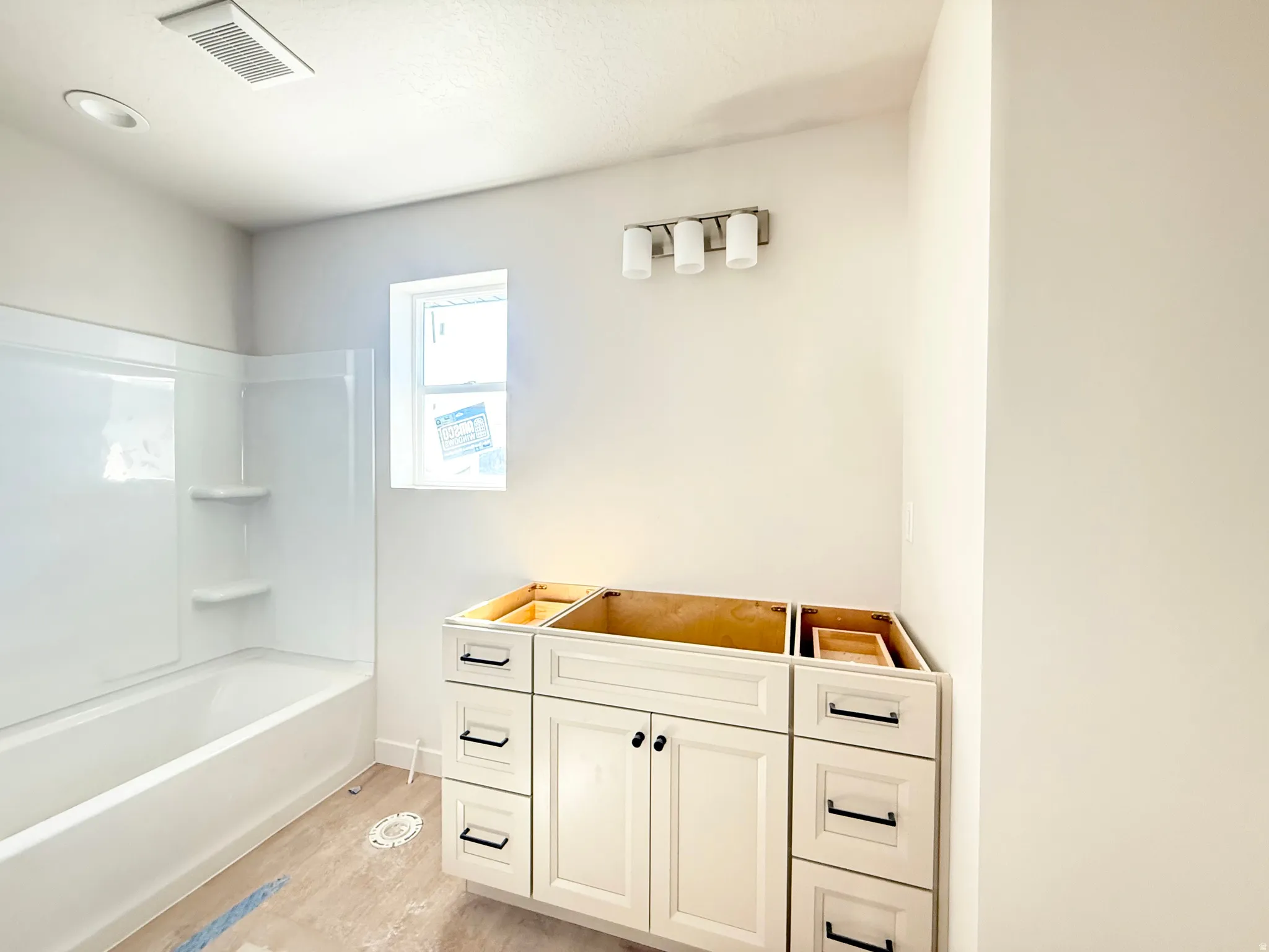 White cabinetry with black hardware, white built-in tub with shelving, and overhead lighting fixtures