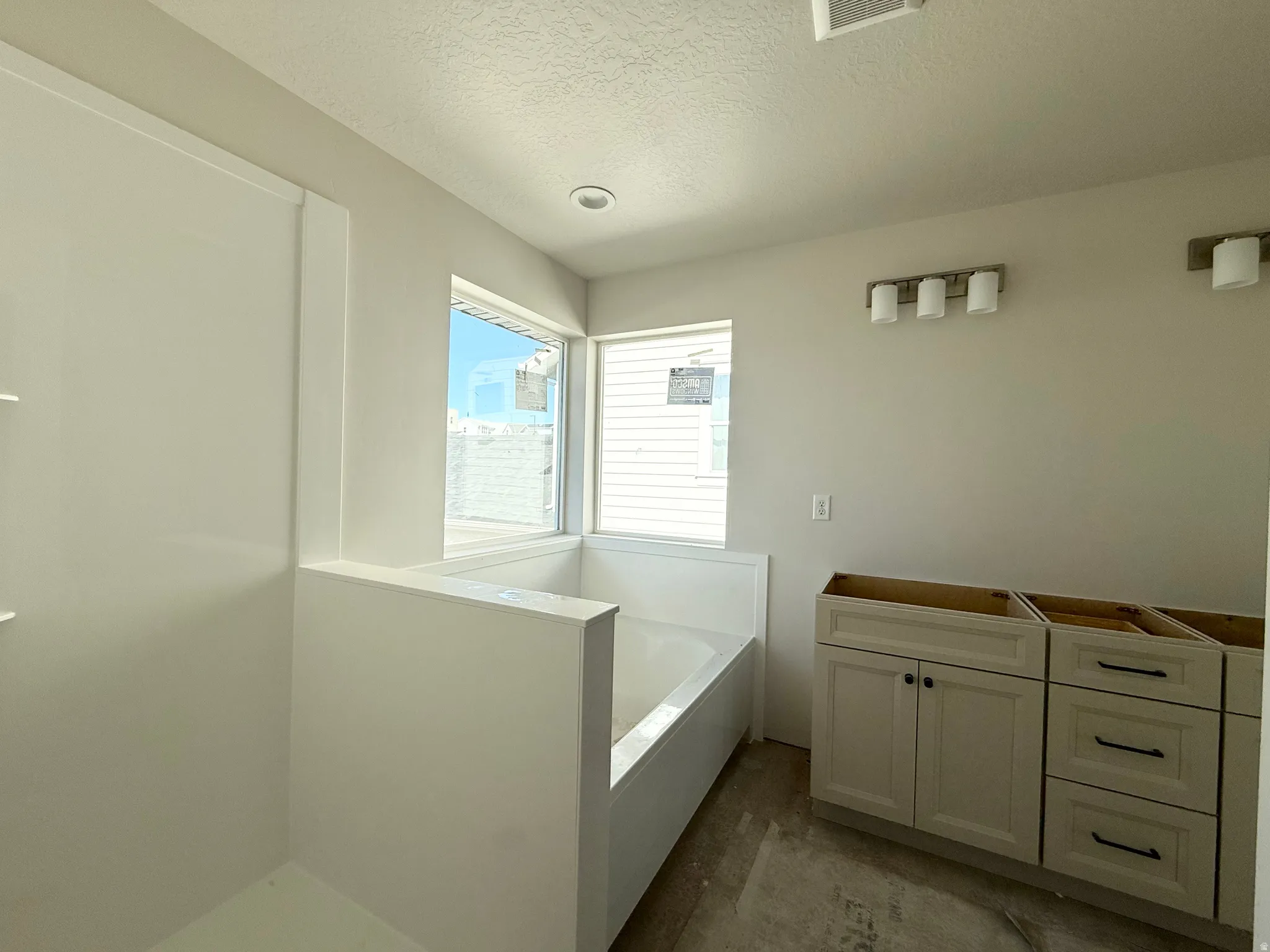 Recessed ceiling lighting, corner windows, built-in tub, separate shower enclosure, and vanity cabinetry with dark hardware