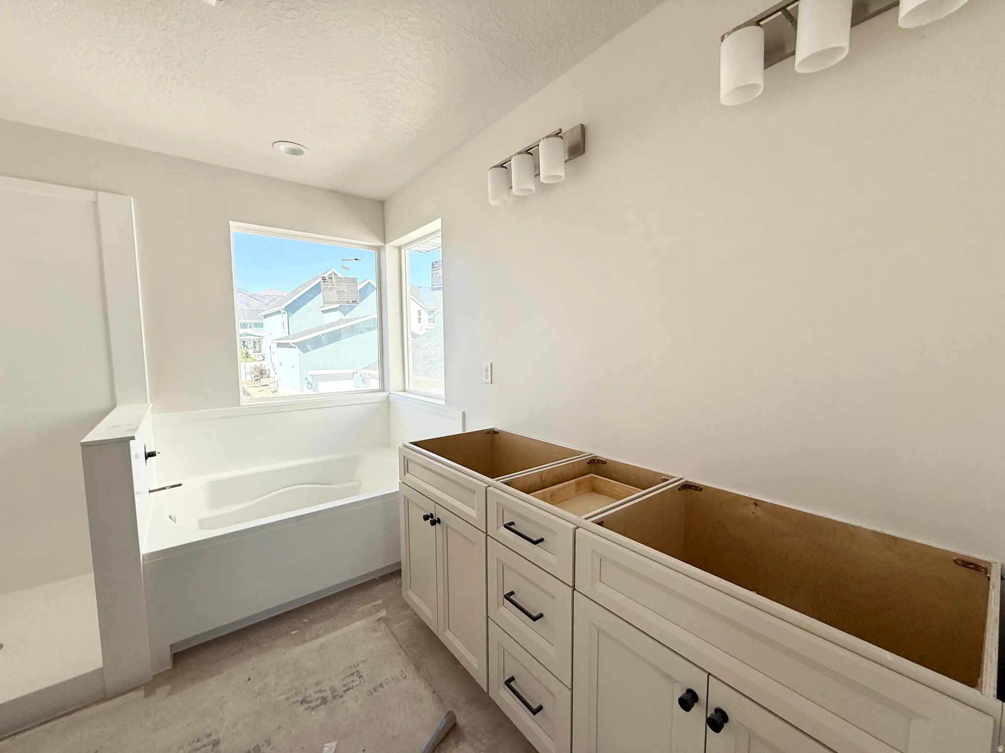 Soaking tub with surrounding windows, walk-in shower, recessed ceiling lighting, and vanity base cabinetry with black hardware