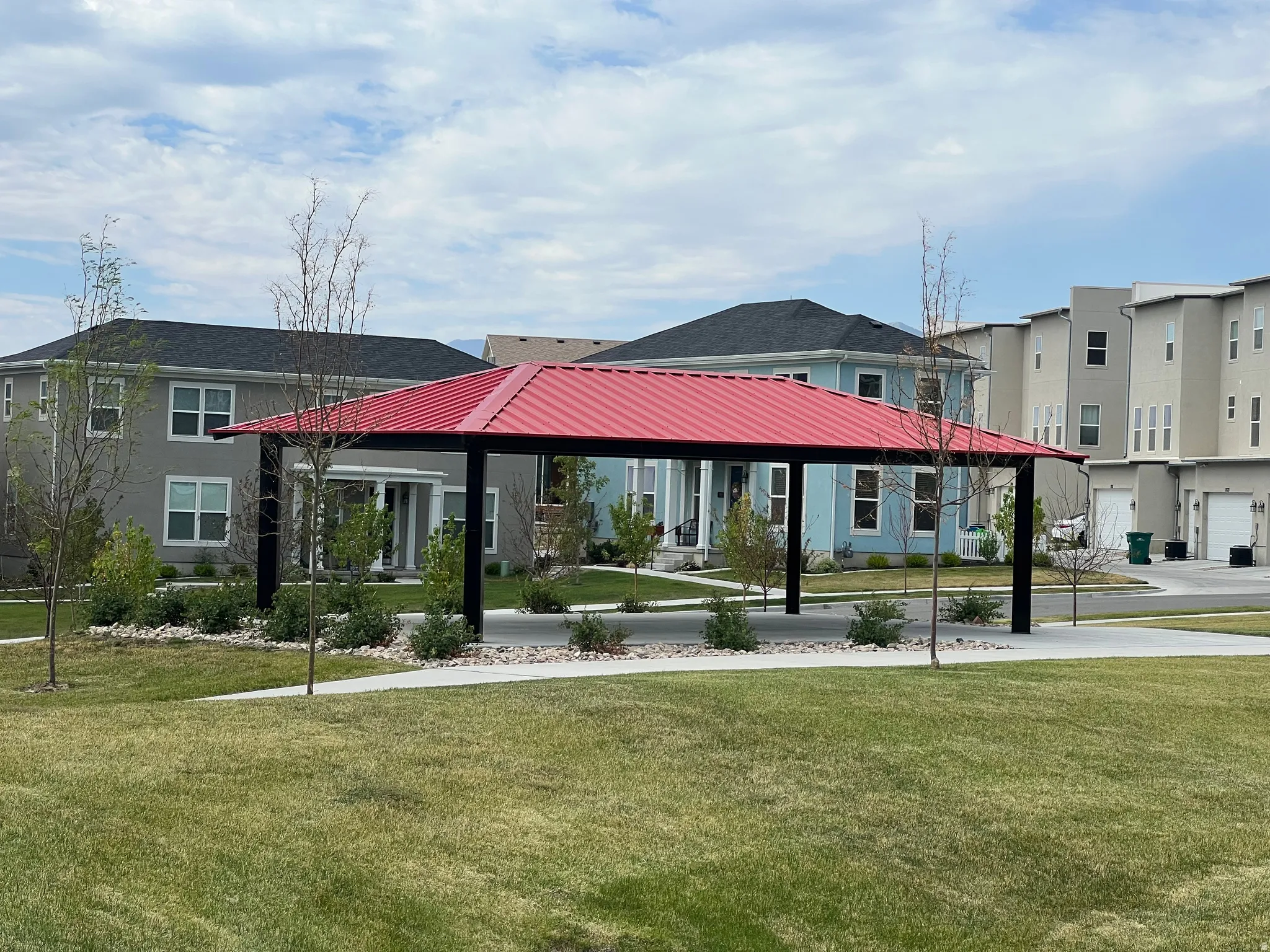 Community pavilion with a red metal roof, surrounded by green lawns and landscaped areas