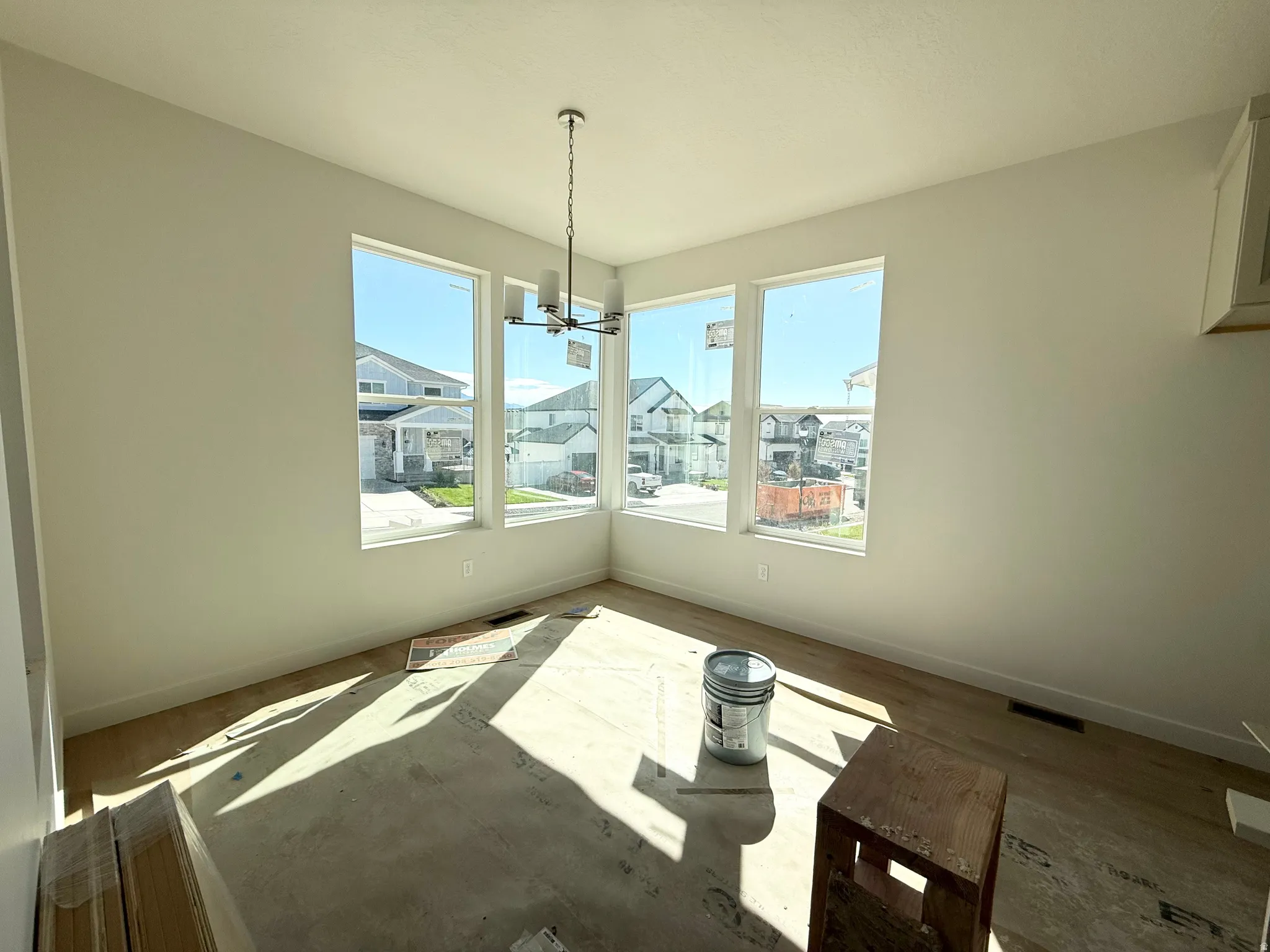 Expansive windows with white trim, contemporary chandelier, light-colored walls, and unfinished flooring