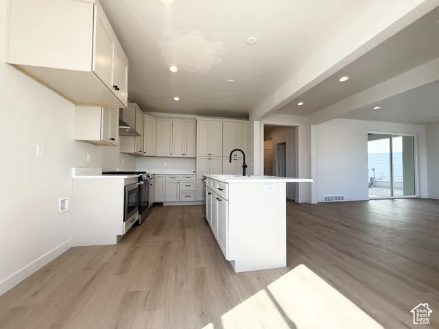 Kitchen featuring white cabinetry, a central island with a sink and breakfast bar, stainless steel appliances, wood-finish flooring, and recessed lighting