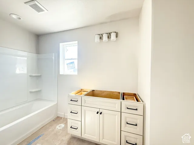 White cabinetry with black hardware, white built-in tub with shelving, and overhead lighting fixtures